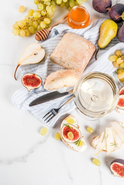 Sandwiches met ricotta of roomkaas, ciabatta, verse vijgen, peren, druiven, walnoten en honing op tafel van wit marmer, met bovenaanzicht van wijnglas copyspace