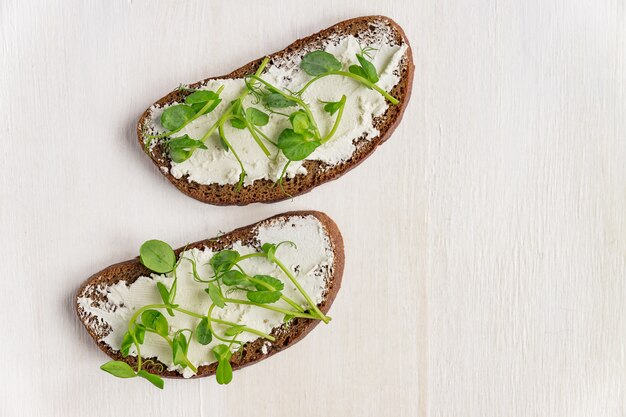 Sandwiches on rye toast with fresh peas microgreen and cream cheese on white background.