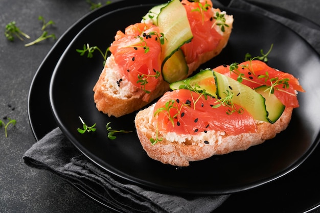 Sandwiches Salmon toast with cream cheese cucumber black sesame and microgreens on black background Seafood Healthy food Photography in low key Top view