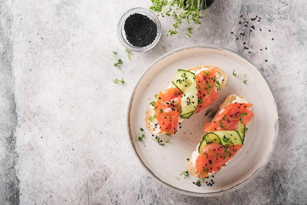 Sandwiches salmon toast with cream cheese cucumber black sesame\
and microgreens on gray concrete table background seafood healthy\
food top view