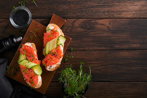 Sandwiches Salmon toast with cream cheese cucumber black sesame and microgreens on old wooden table background Seafood Healthy food Photography in low key Top view