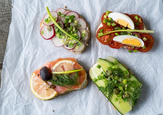 Sandwiches or tapas prepared with cream cheese , vegetables and salmon, over white paper background.