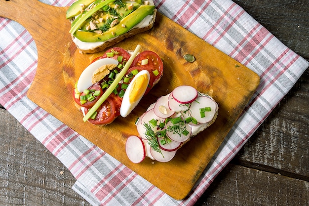 Sandwiches or tapas with  vegetables, on cutting board, over wooden background. 