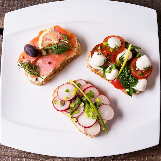 Sandwiches or tapas with vegetables and salmon, on a plate, over wooden background.