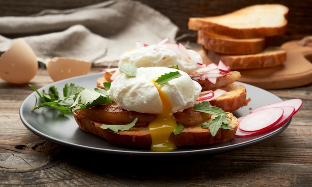 Sandwiches on a toasted white slice of bread with poached eggs, green leaves of arugula and radish in a round plate