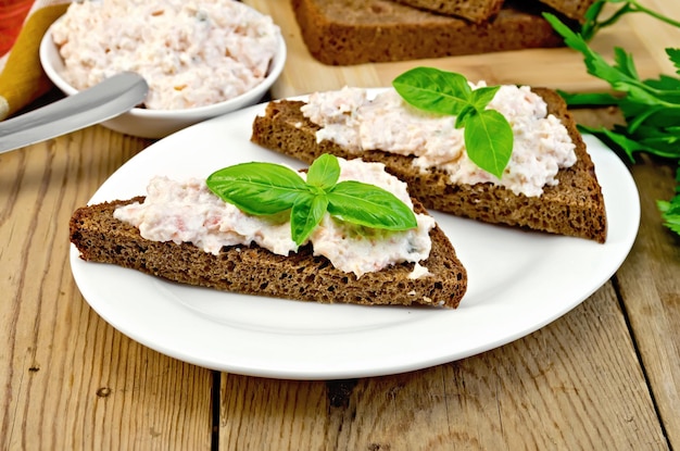 Panini su due fette di pane di segale con crema di salmone e maionese, basilico, coltello, tovagliolo sui taglieri di legno