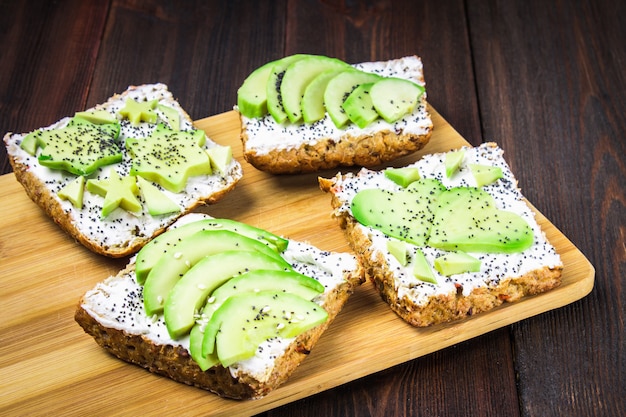 Sandwiches van brood met plakjes, sterren, harten van avocado en kwark op houten achtergrond.