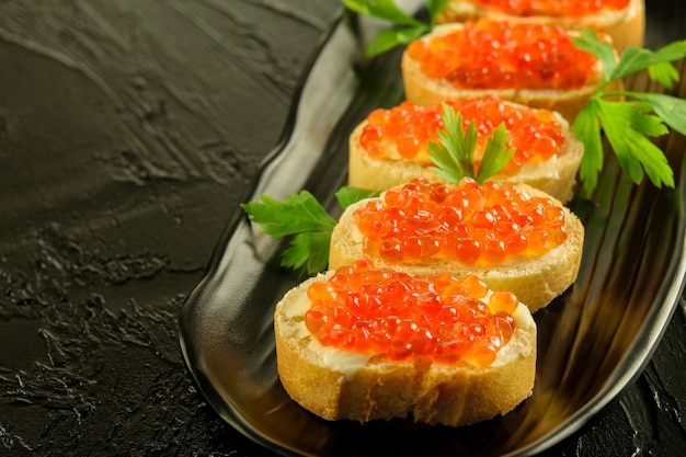 Foto sandwiches van vers wit brood met boter en verse rode kaviaar op de zwarte schotel