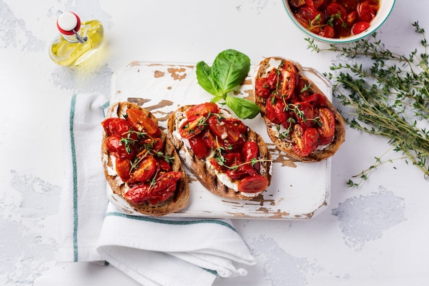 Sandwiches with baked cherry tomatoes and cottage cheese and herbs on a light surface. Top view.