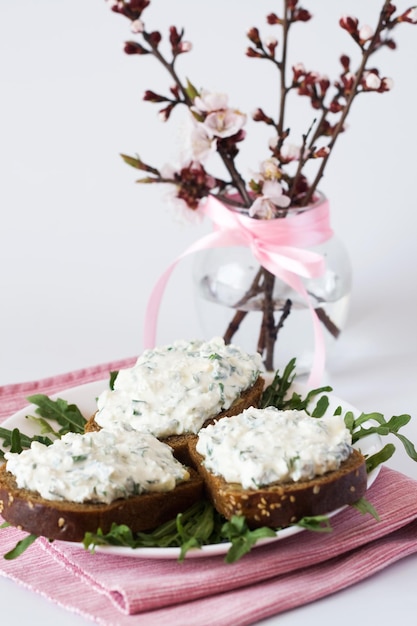 Sandwiches with cheese and herbs on a plate next to a vase with kidneys