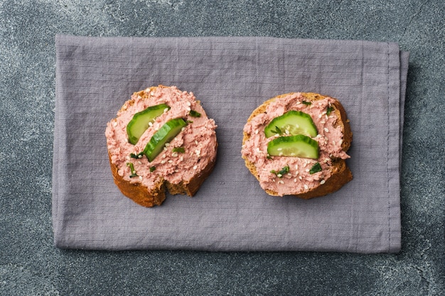 Sandwiches with chicken pate and cucumber on dark table.