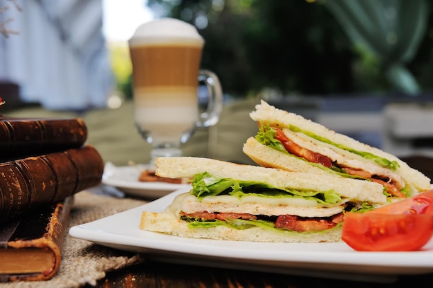 Sandwiches with chicken, tomato and salad on a wooden background on a latte background and old books