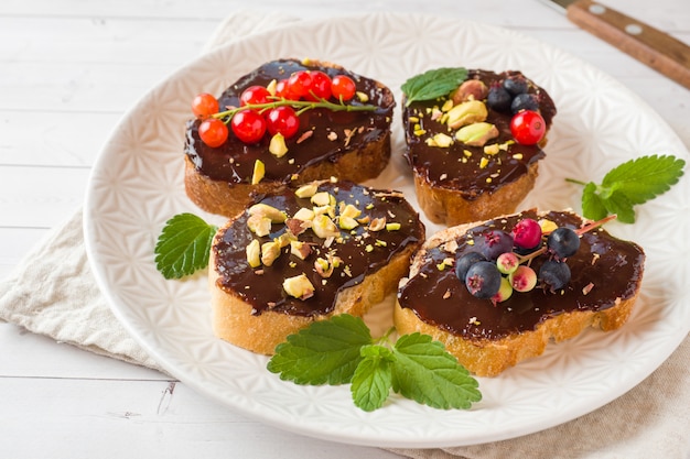 Бутерброды с шоколадной пастой, фисташками и свежими ягодами на тарелке.