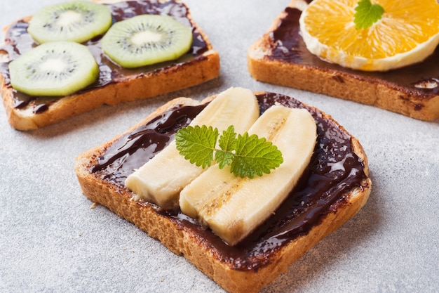 Sandwiches with chocolate paste and various fruits on a gray table. 