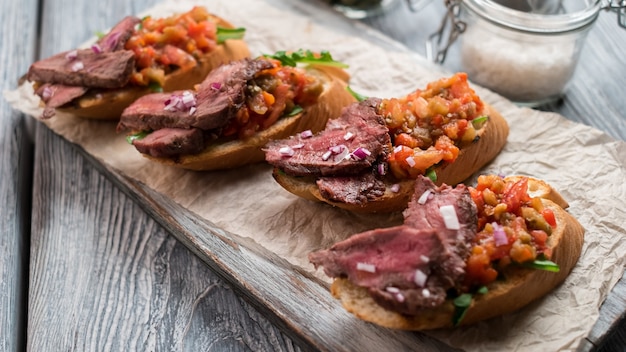 Sandwiches with cooked meat. Mixture of chopped vegetables. Delicious bruschetta with veal. Savoury snack on wooden board.