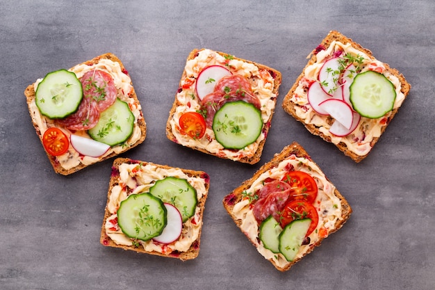 Sandwiches with cream cheese, vegetables and salami. Sandwiches with cucumber, radish, tomatoes, salami on a gray background, top view. Flat lay.