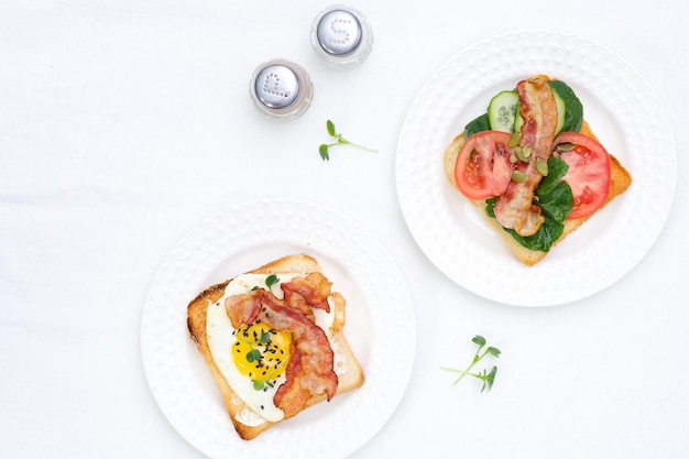 Сэндвичи с жареными яйцами, жареной ветчиной, помидорами, огурцами, перцем на белом фоне.