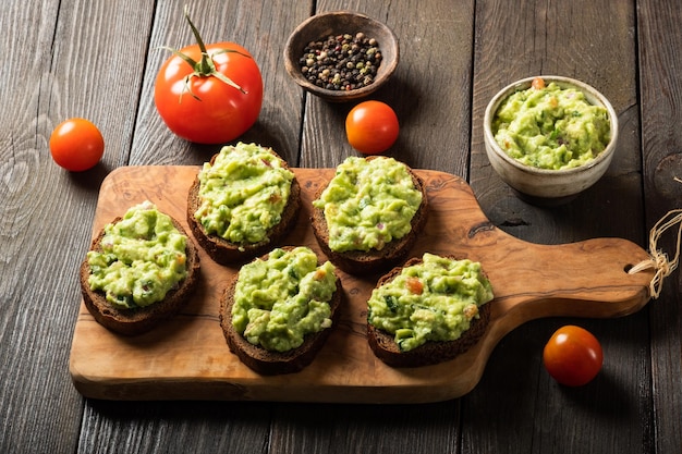 Sandwiches with guacamole sauce on a cutting board over old wooden background