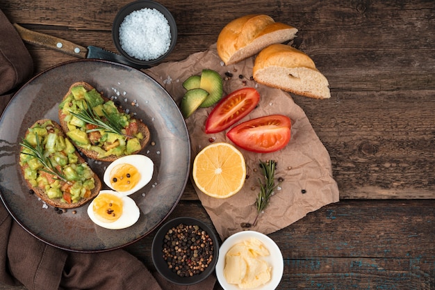 Photo sandwiches with guacamole, tomatoes, rosemary, lemon, butter on a wooden background. top view with copy space. the concept of healthy food.