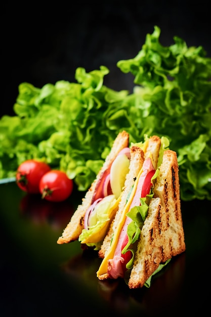 Бутерброды с ветчиной, листьями салата и свежими овощами на темном фоне
