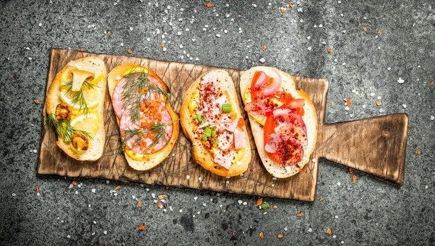 Sandwiches with meat, salami, seafood and fresh vegetables on rustic table.