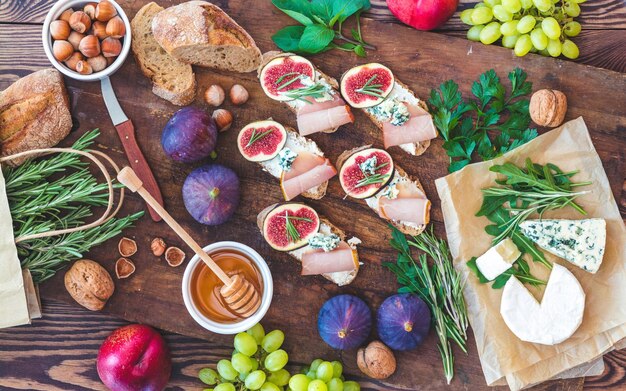 Sandwiches with ricotta fresh figs prosciutto rosemary and blue cheese walnuts and honey on rustic wooden board over black backdrop top view Delicious fruity breakfast Toned