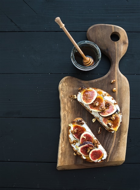 Sandwiches with ricotta, fresh figs, walnuts and honey on rustic wooden board over black backdrop