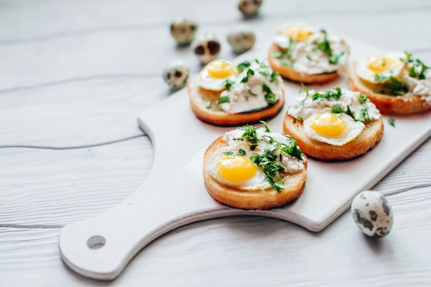 Sandwiches with ricotta and quail eggs with greens on a white board on the table