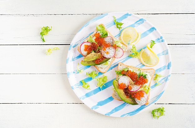 Sandwiches with salmon red caviar with sliced avocado and radish. Sandwich for lunch. Premium food. Overhead, top view, flat lay