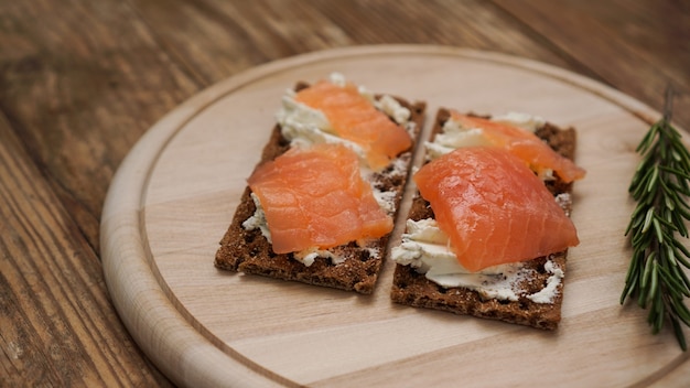 Sandwiches with salmon on wooden cutting board, close up view