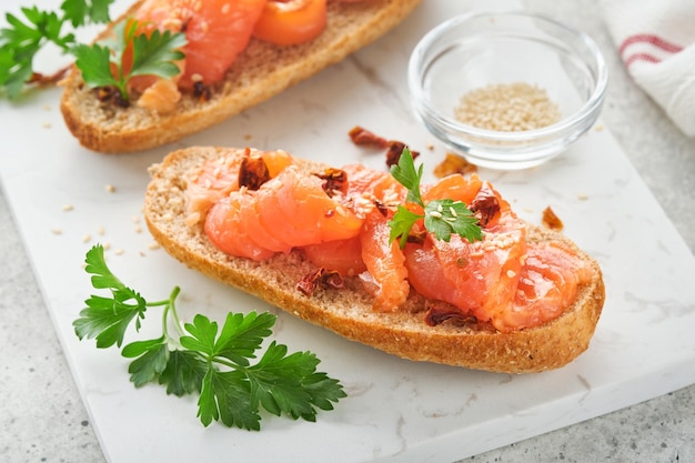 Sandwiches with salted salmon Open sandwiches from cereal or whole grain rye bread with salted salmon sesame seeds and dried tomato on white marble stand Seafood Healthy food Scandinavian cuisine