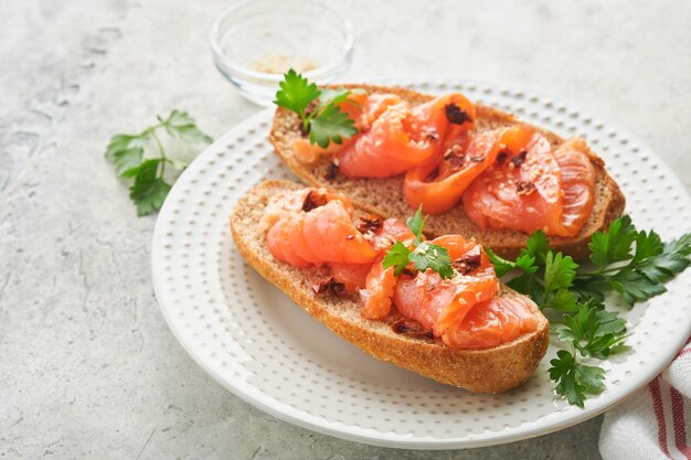 Sandwiches with salted salmon Open sandwiches from cereal or whole grain rye bread with salted salmon sesame seeds and dried tomato on white marble stand Seafood Healthy food Scandinavian cuisine