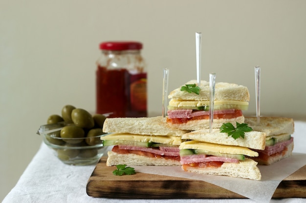Sandwiches with sausage, meat, cheese and fresh vegetables on a table with olives and ketchup.