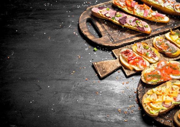 Sandwiches with seafood, meat and vegetables on fresh bread. On the black chalkboard.