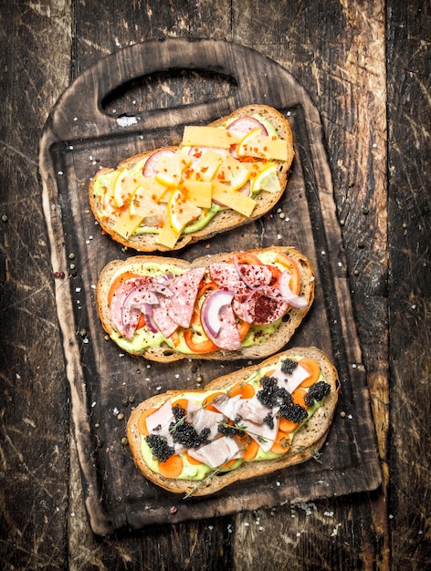 Sandwiches with seafood, salami, cheese and vegetables on wooden table.