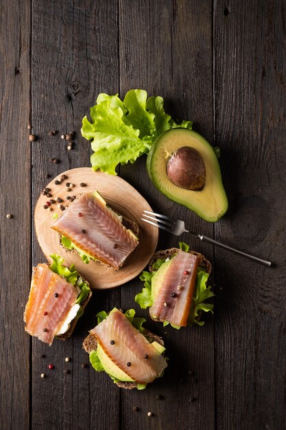 Sandwiches with smoked fish and avocado on a board on a dark background
