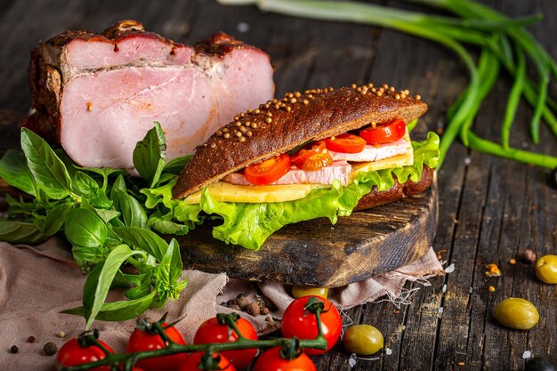 sandwiches with smoked meat or pork, with cherry tomatoes, herbs and spices, on a black wooden