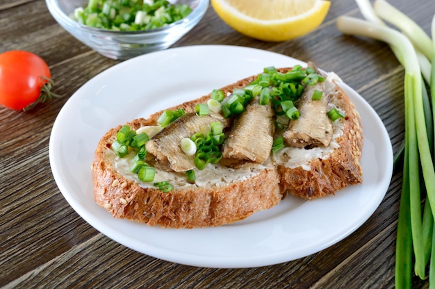 Sandwiches with smoked sprat, butter and green onions on the wooden background. Danish cuisine. Close-up.