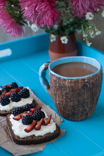 Panini con formaggio dolce e bacche, una tazza di caffè in tavola di legno blu