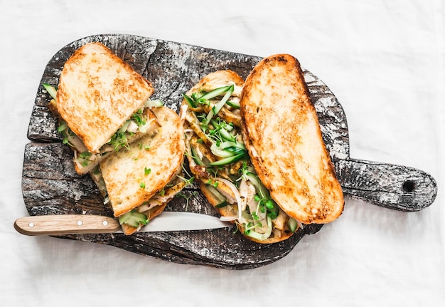 Sandwiches with turmeric fried chicken cucumber microgreens and homemade mustard mayonnaise sauce on a wooden cutting board on a light background Delicious tapas snack breakfast