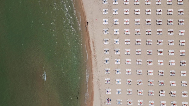 Una spiaggia sabbiosa si estende lungo il mare adornata con lettini vuoti vista aerea