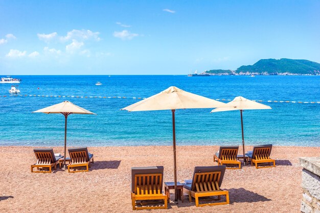 Песчаный пляж в Свети-Стефане с шезлонгами и зонтиками в летний день, Черногория