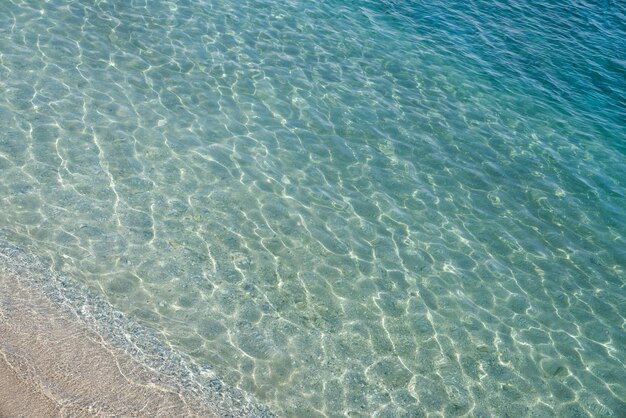 Sandy beach that goes under sea surface of water, sun glare on water surface