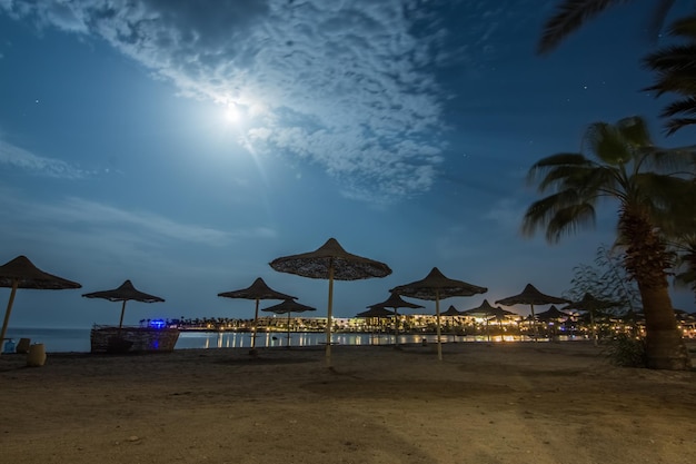 Sandy beach with beach umbrellas and a bright moon in the night