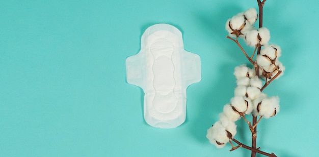 Sanitary napkin with wings and cotton flowers on mint green color or Tiffany Blue background.top angle view