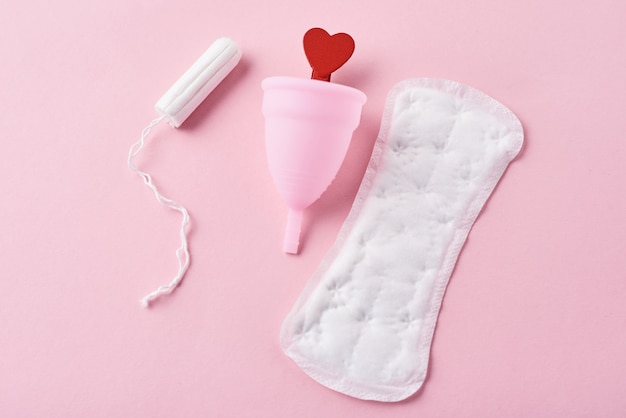 Sanitary pad, menstrual cup, tampon and red wooden heart 