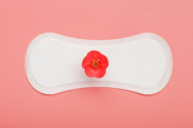 Sanitary pad on a pink background with a red flower. Free space for text.