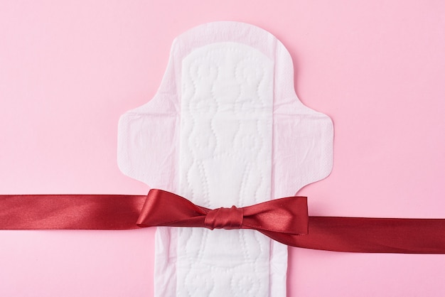 Sanitary pad and red ribbon on a pink surface