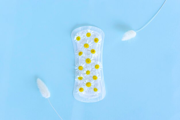 A sanitary pad with chamomile flowers on it lies on a yellow background. Menstruation days. Hygiene and freshness concept