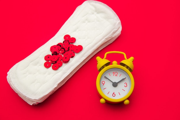 Sanitary pads and alarm clock on red